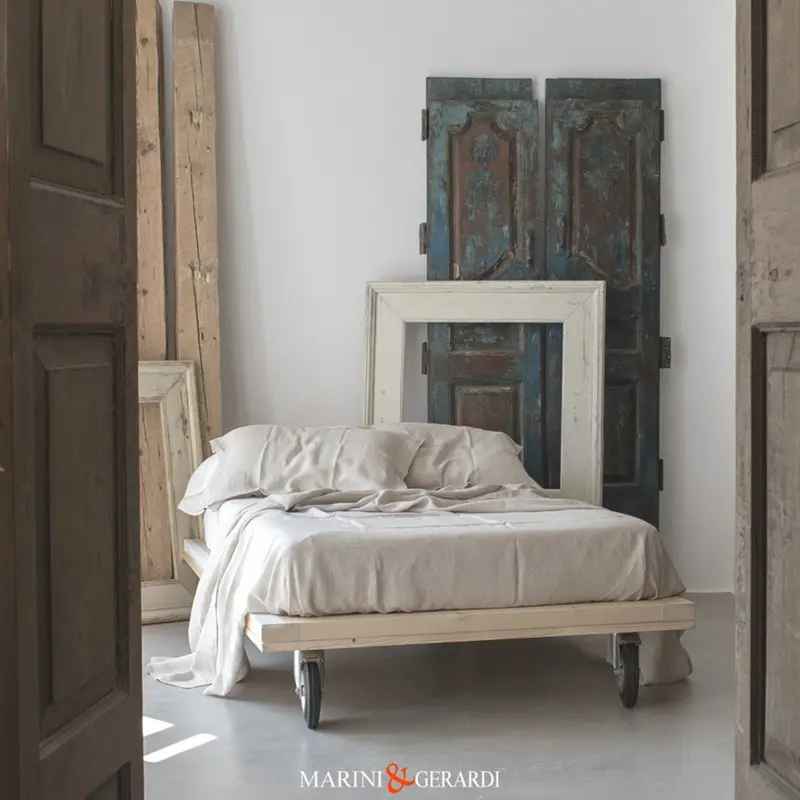 Lenzuola in lino bianche su letto ruote industriali porte e arredo interni in legno.
